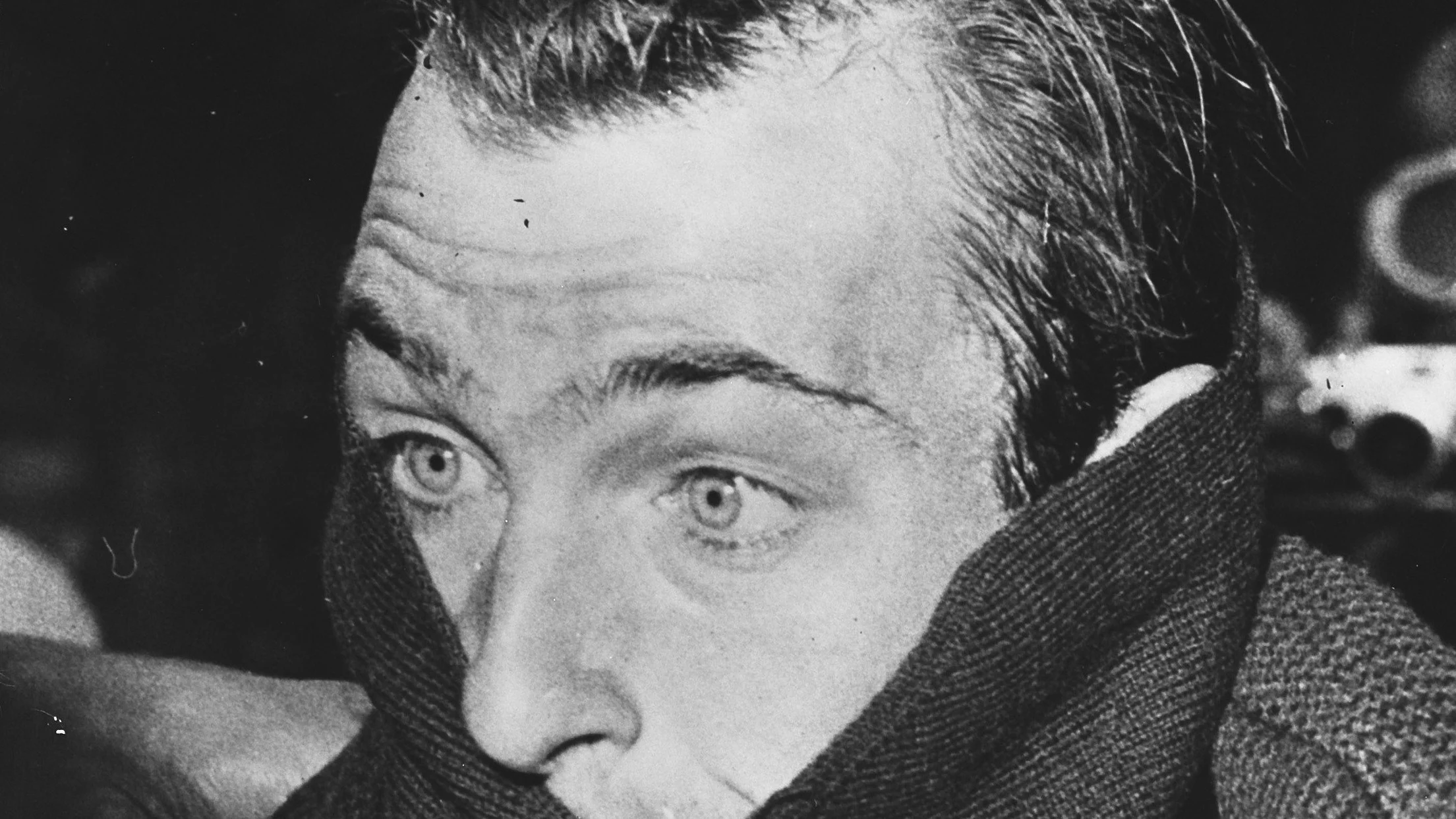 Foto in bianco e nero: primo piano di Charly Gaul, capelli spettinati e occhi spalancati, avvolto fino al naso nel collo alto di una maglia di lana.